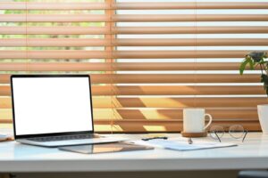 wooden blinds with computer and coffee cup on desk in front of them