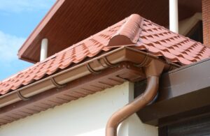 Close-up of roof gutter and downspout pipe next to clay tile roof.