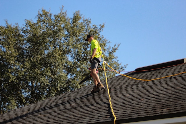 Man on brown tile roof with harness carries leaf blower